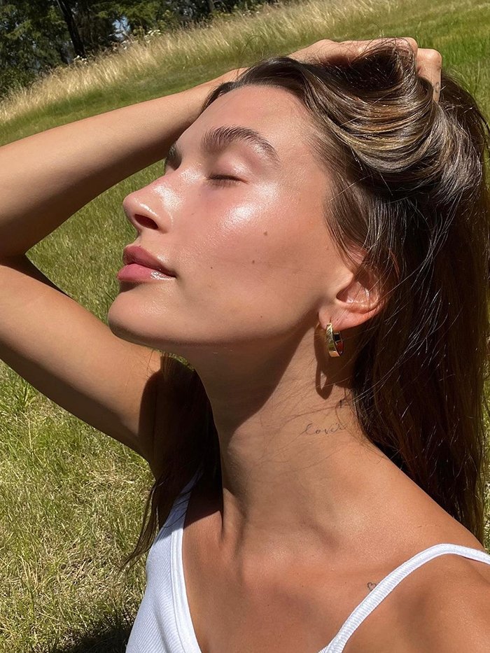 Woman applying heat-proof summer makeup with glowing skin, perfect eyeliner, and natural lip stain under bright sunlight
